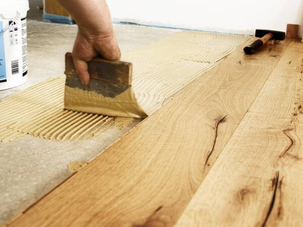 L'artisan carreleur de Bordeaux pose un parquet avec une brosse à colle.